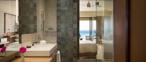 A modern bathroom with a large mirror, a shower, and a view of the beach.