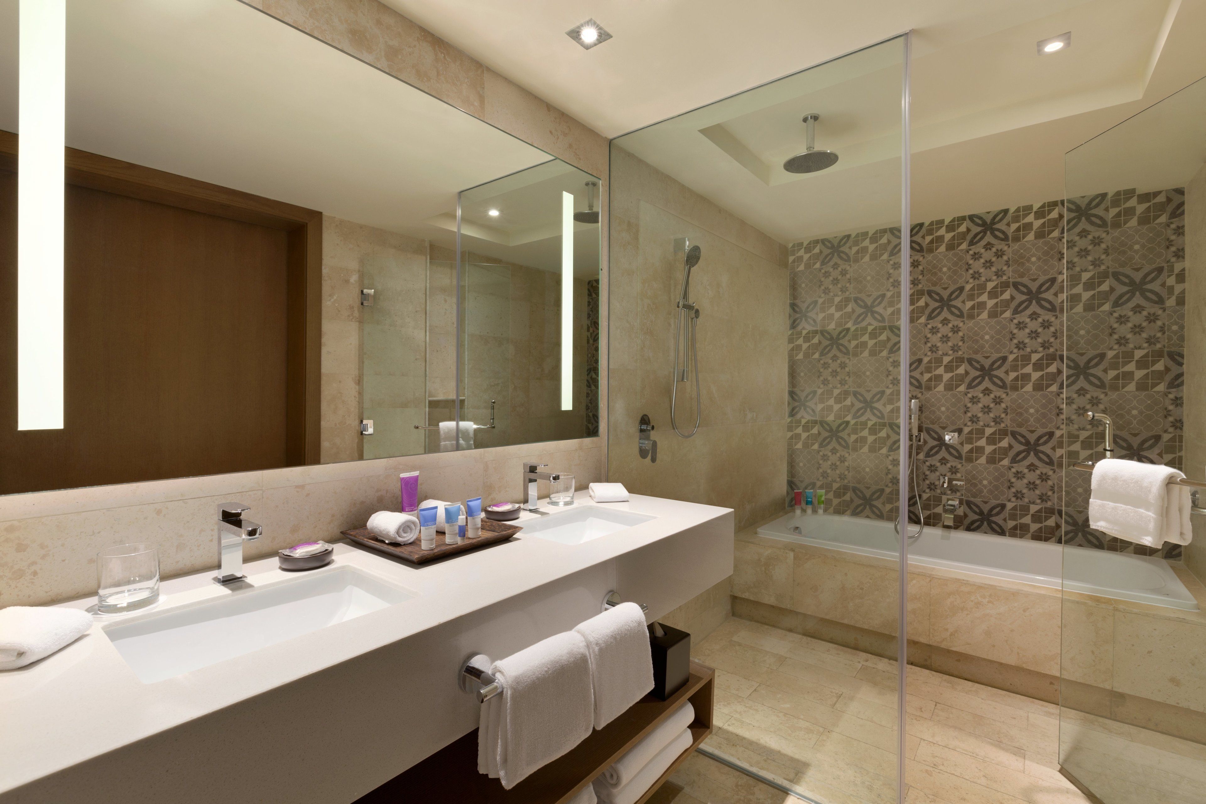 A modern bathroom with a large mirror, two sinks, a shower, and a glass-enclosed shower area.