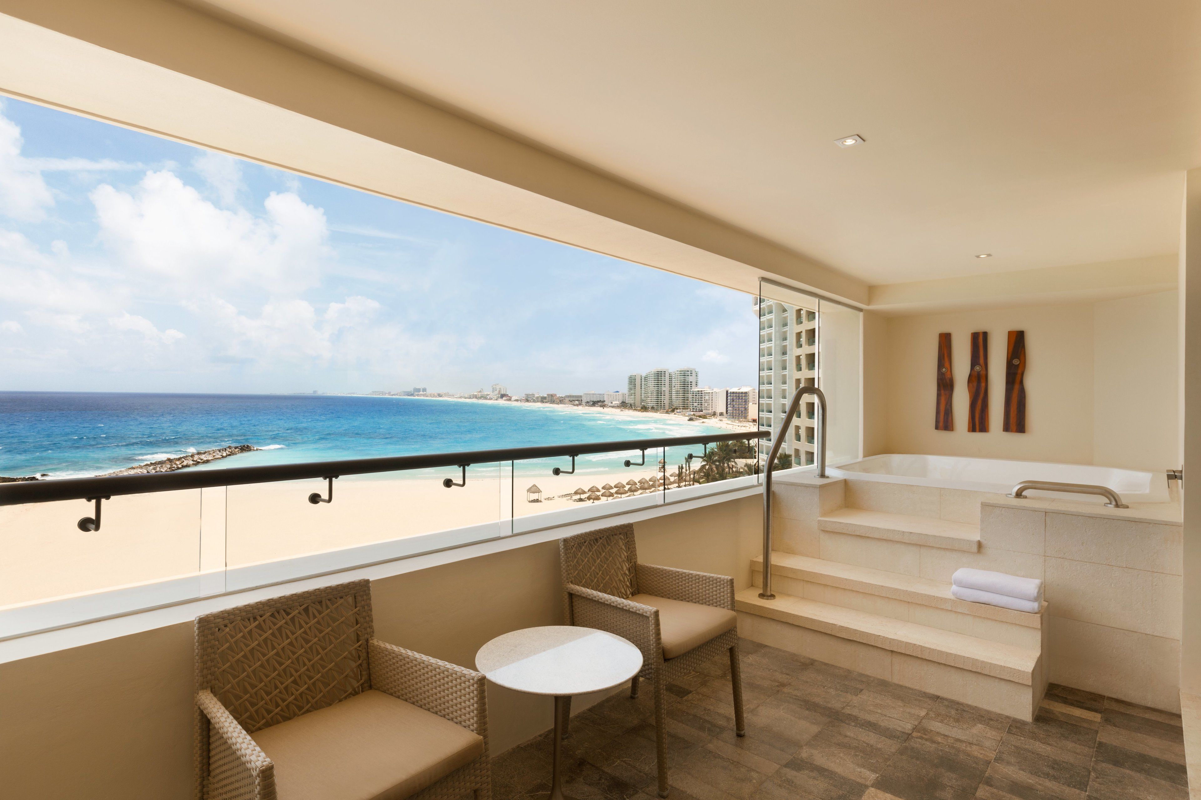 A balcony with wicker furniture, a view of the beach, and a bathroom with a bathtub and towel.