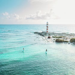 Explore the tranquil coastal scene with a historic lighthouse and calm waters perfect for paddleboarding.