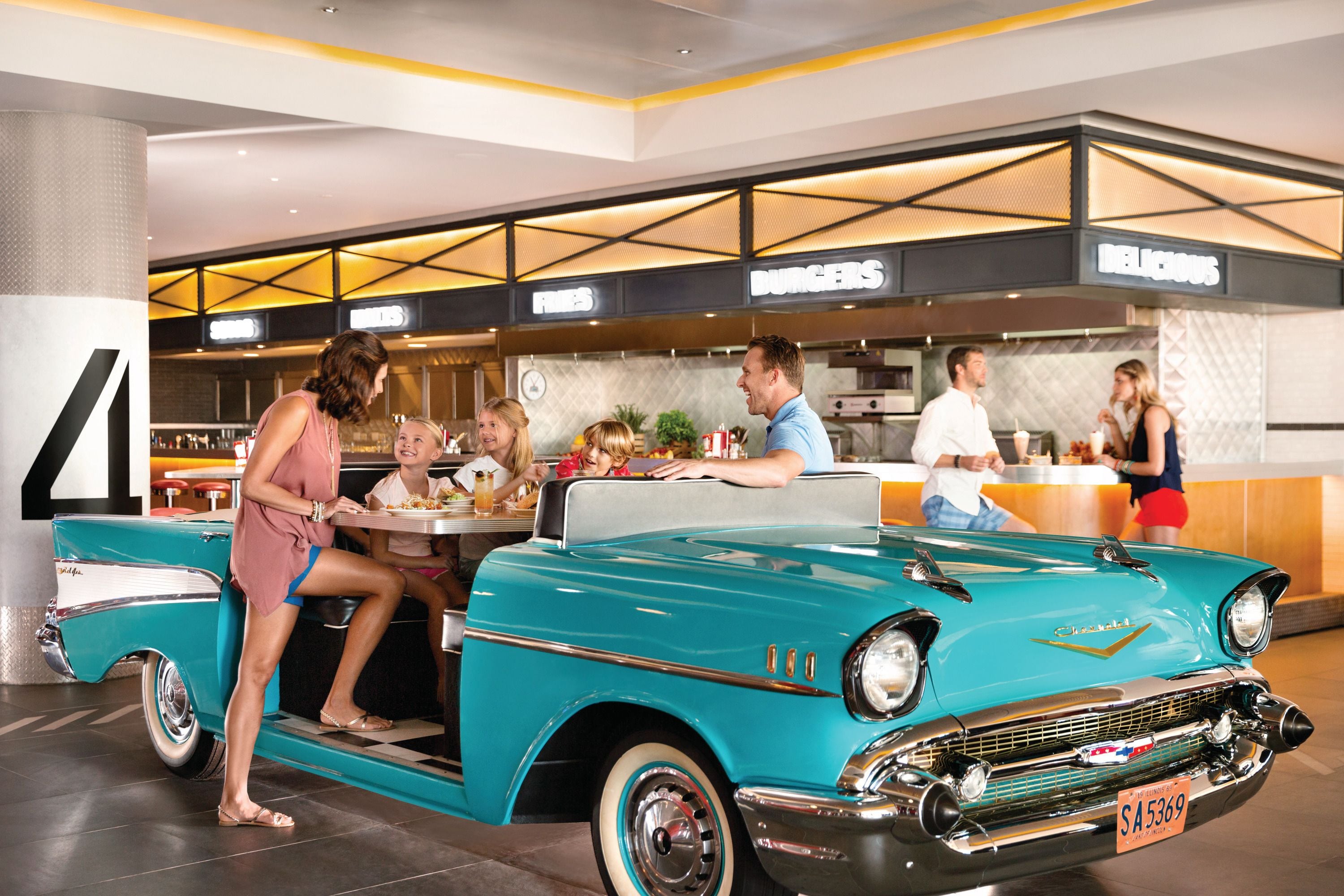 A vintage car in a showroom with a modern restaurant in the background.