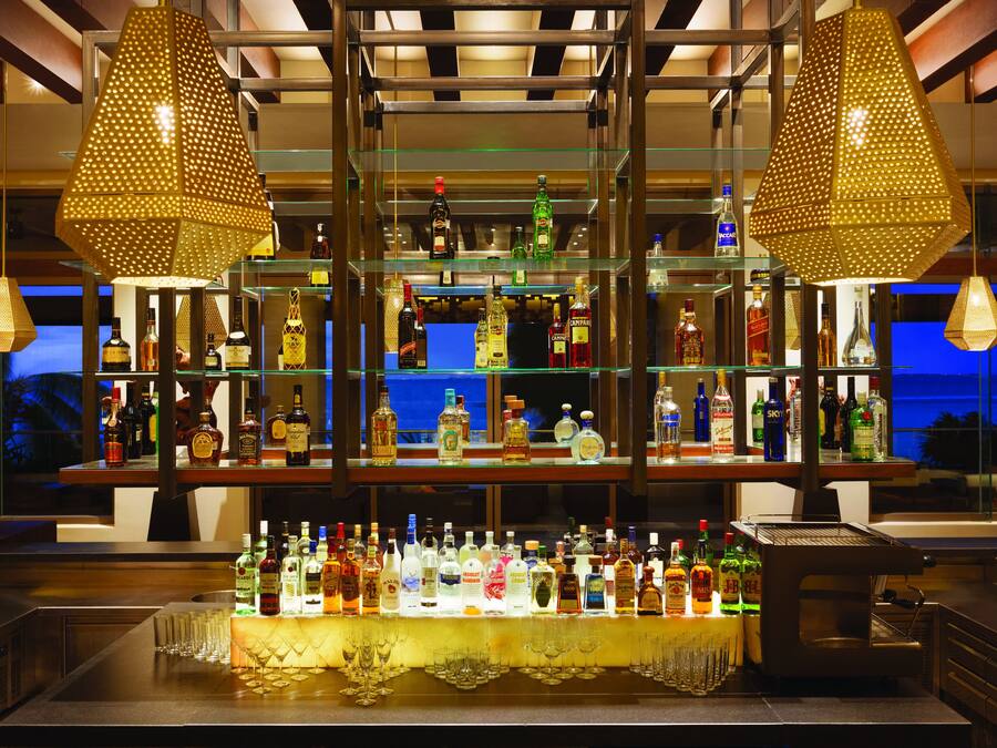 A bar with multiple shelves of liquor bottles, a coffee machine, and hanging pendant lights.