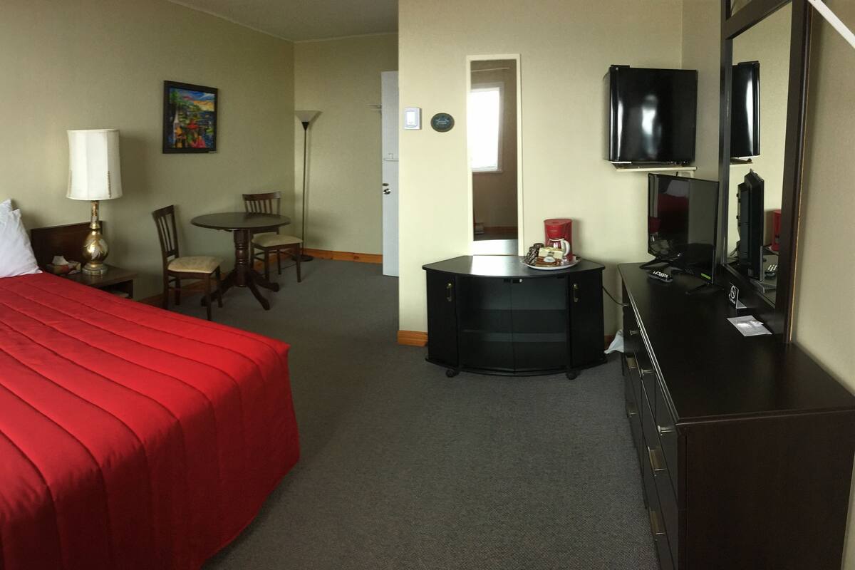 A hotel room with a large bed, a desk, a chair, a lamp, a TV, and a dresser.