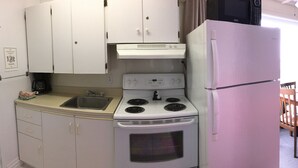 A compact kitchen with white cabinets, a stove, a sink, and a refrigerator. - Motel Sainte-Flavie (Sainte-Flavie)