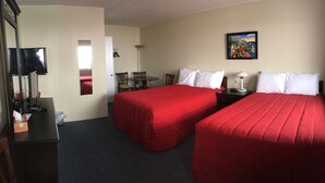 A hotel room with two beds, a desk, a chair, a table, a TV, and a painting on the wall. - Motel Sainte-Flavie (Sainte-Flavie)