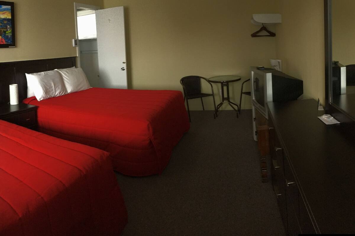 A hotel room with two beds, a desk, a chair, a TV, and a painting on the wall.