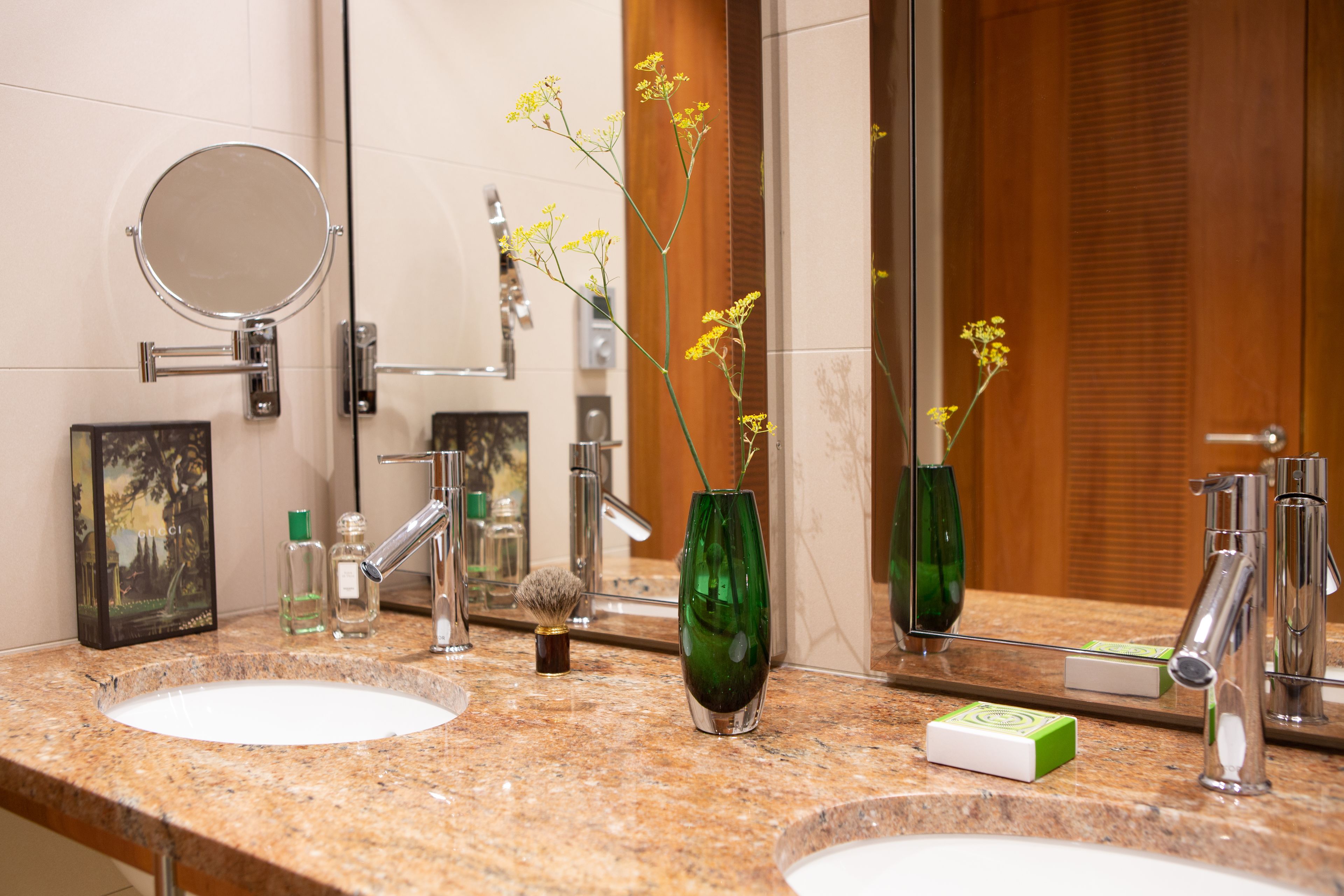 Un baño con dos lavamanos, un espejo y un florero verde con flores amarillas.