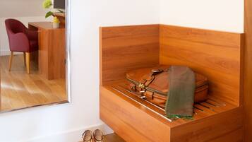 Habitación en esquina con un banco de madera, un par de zapatos, un bolso y un espejo que refleja un escritorio y una silla.