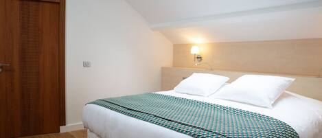 A bedroom with a skylight, a bed with a patterned bedspread, a wooden wardrobe, and a wall-mounted light fixture.
