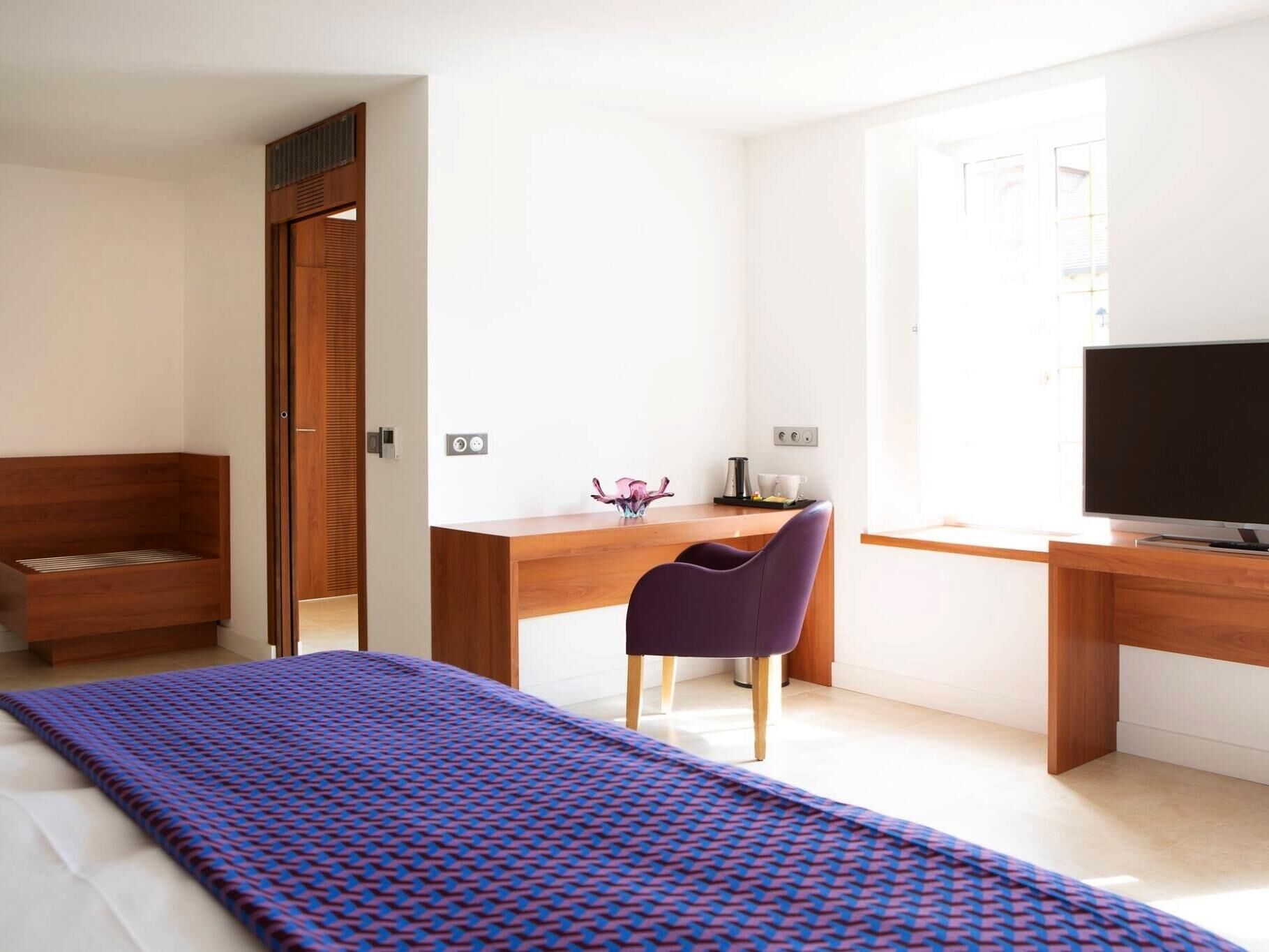 Een moderne slaapkamer met een bed, een bureau, een stoel en een televisietoestel.