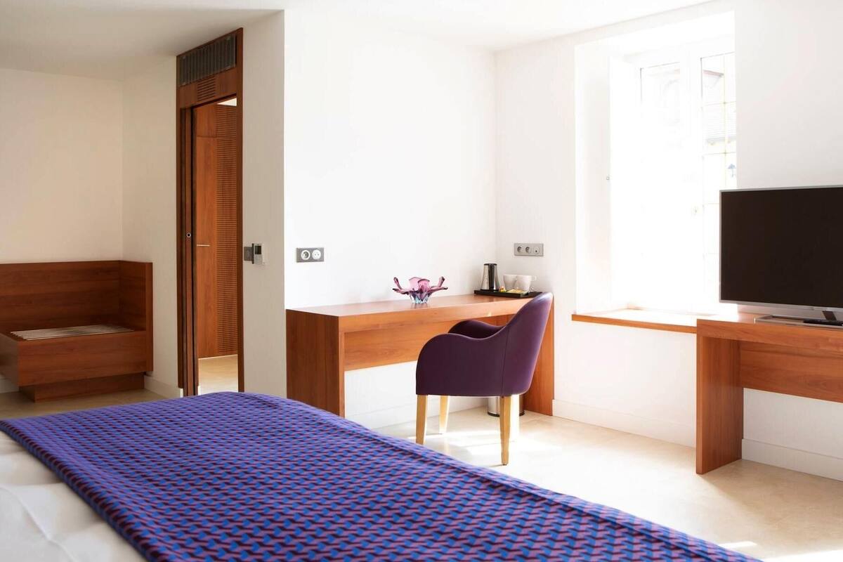 A modern bedroom with a bed, a desk, a chair, and a television.