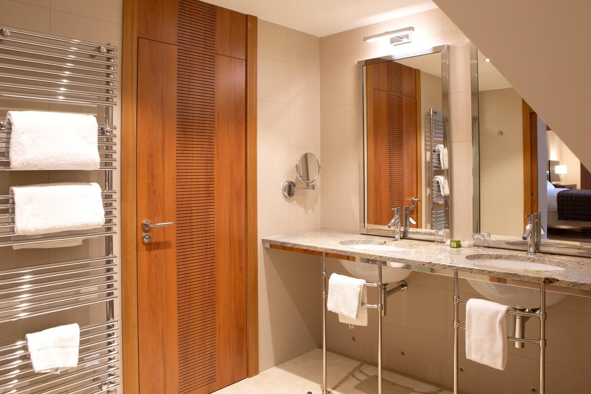 A modern bathroom with a wooden vanity, two sinks, a large mirror, and towel racks.