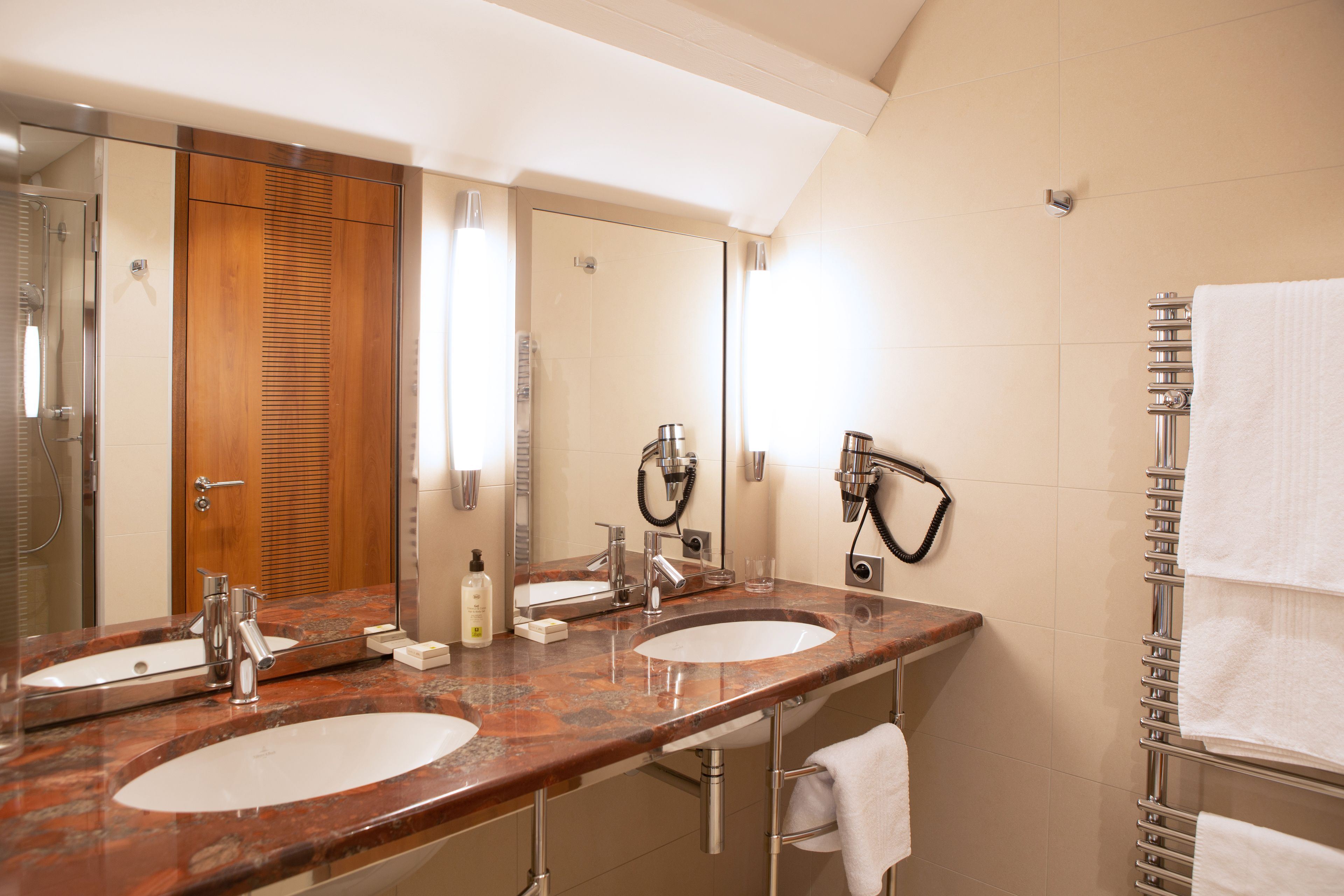 Een badkamer met twee wasbakken, een spiegel, een handdoekhouder en een douche.
