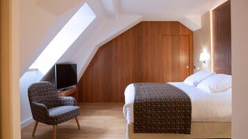 Un dormitorio con techo inclinado, una cama con manta estampada, una silla y un televisor sobre un soporte de madera.