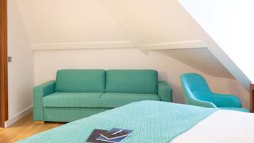 Une pièce avec un canapé vert, un fauteuil turquoise et un lit recouvert d’une couvre-lit à motifs.