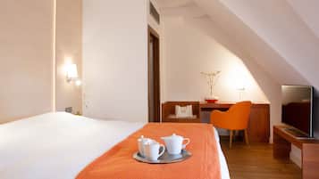 Ein Hotelzimmer mit Bett, Schreibtisch mit Stuhl, Fernseher und Tablett mit Tassen und Teekanne.