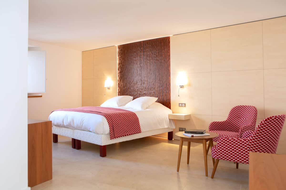 A modern hotel room with a large bed, two bedside tables, a small table, and two patterned chairs.