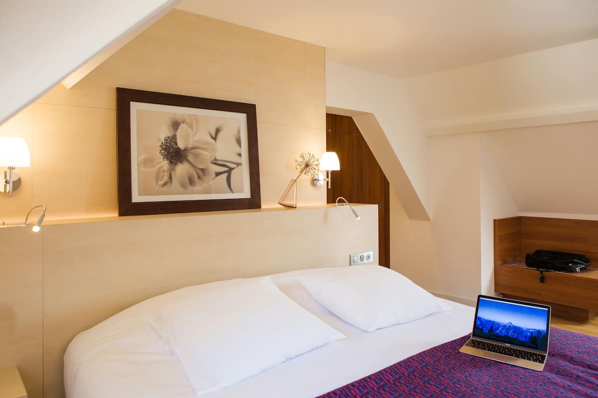 A hotel room with a bed, a laptop, a framed artwork, and a wooden nightstand.