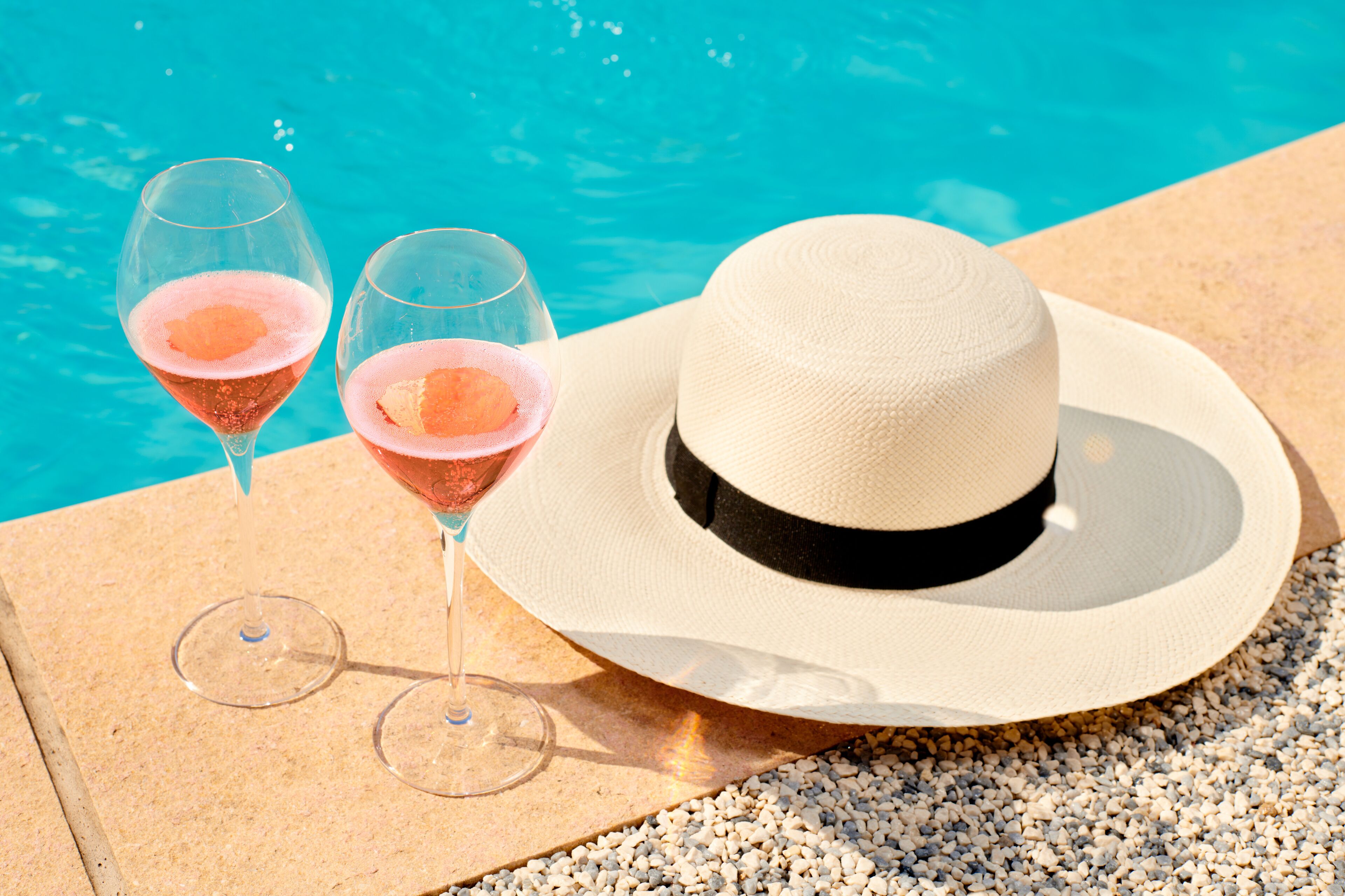 A poolside setting with a hat and two glasses of pink drink.