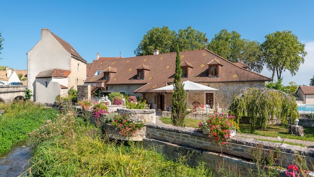 Un bâtiment en pierre avec un toit en tuiles, un petit jardin fleuri et un ruisseau.