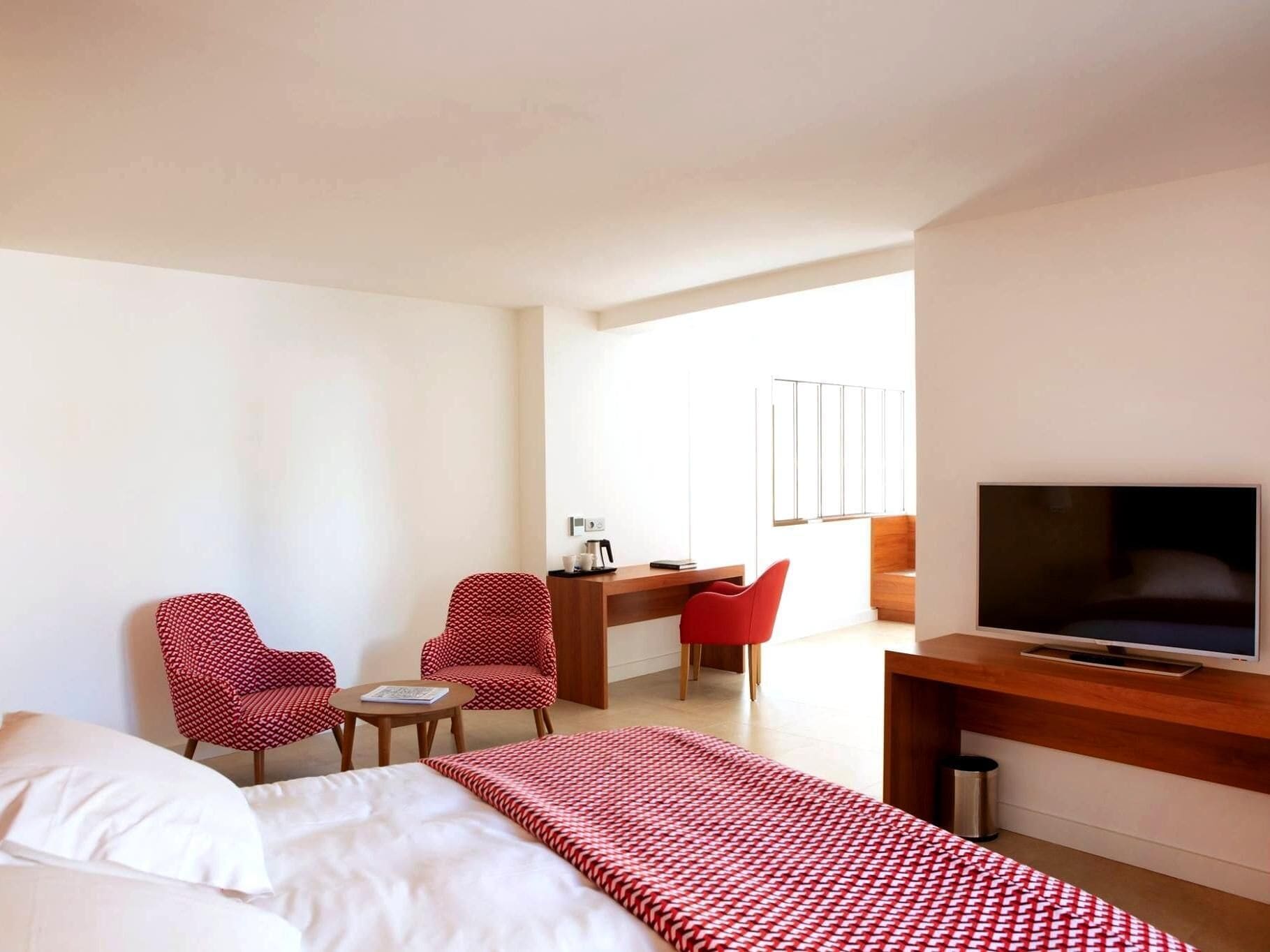Een hotelkamer met een bed, een bureau, twee stoelen, een televisie en een raam.