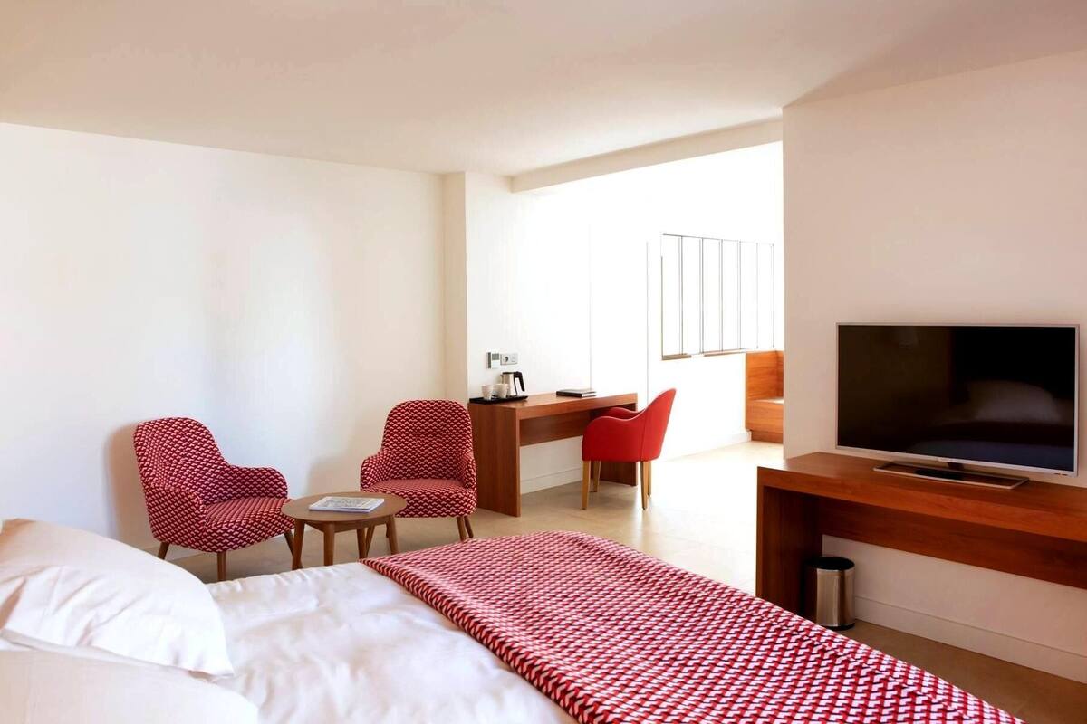 A hotel room with a bed, a desk, two chairs, a television, and a window.