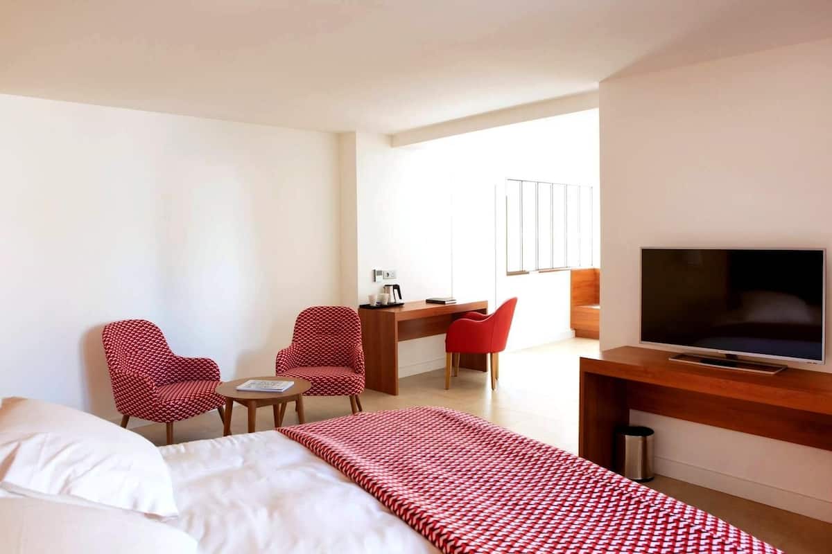 A hotel room with a bed, a desk, two chairs, a television, and a window.