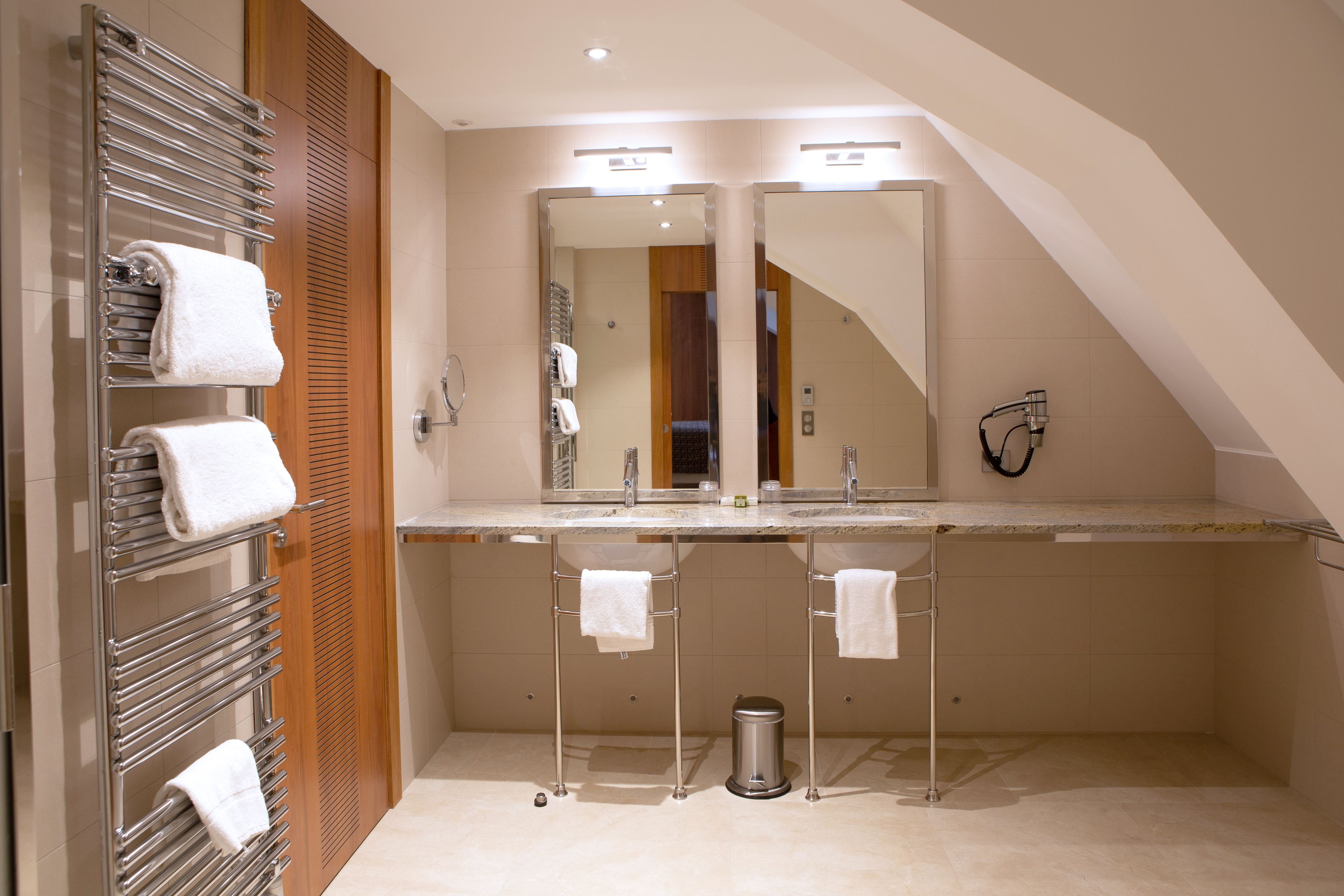 A modern bathroom with a large mirror, two towel racks, a sink, and a trash can.