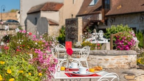 Une table dressée à l’extérieur, ornée d’une rose rouge, de vaisselle blanche et d’un verre de jus d’orange.