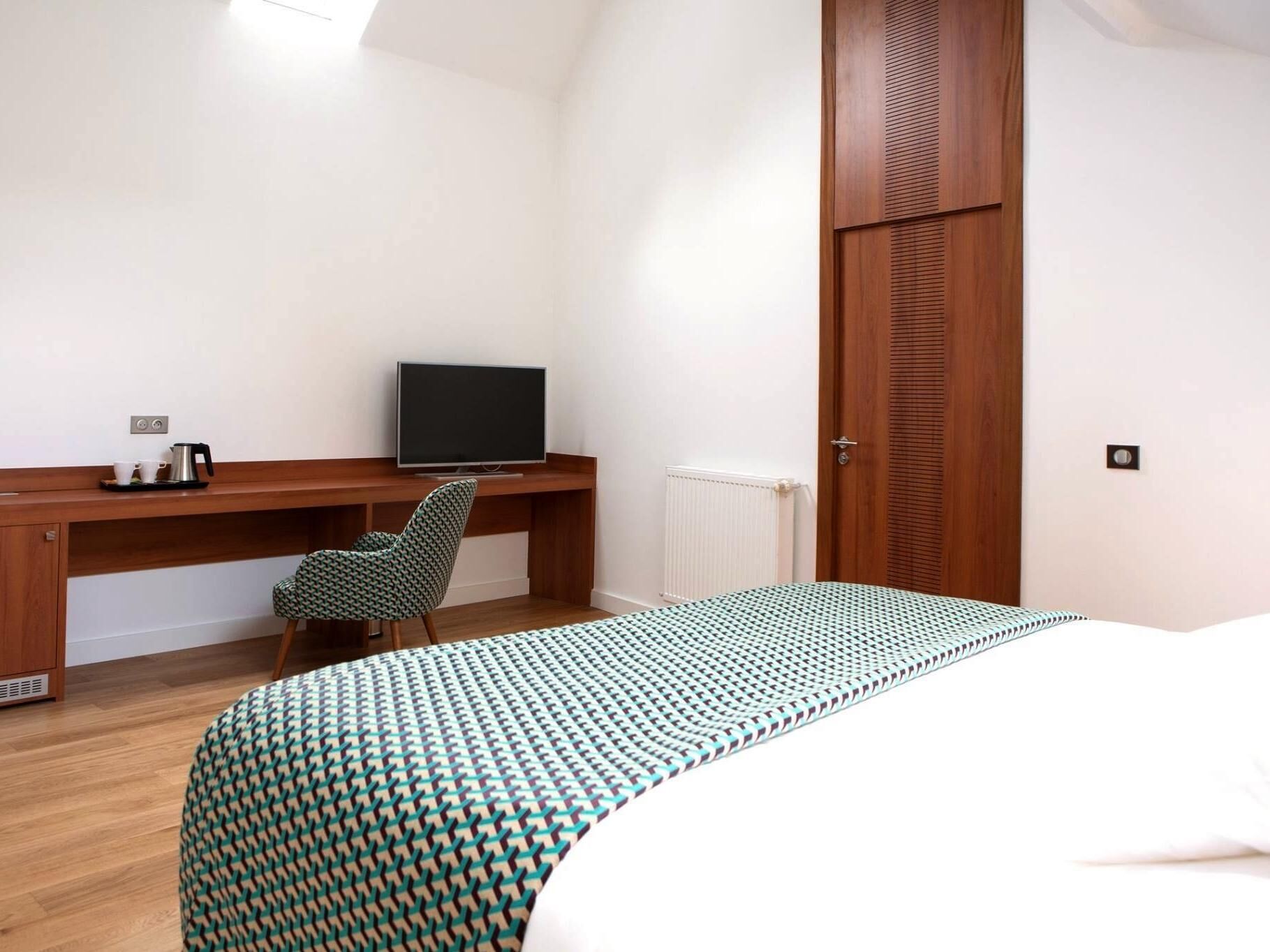 Een slaapkamer met een bed, een bureau met een televisie, een stoel en een radiator.