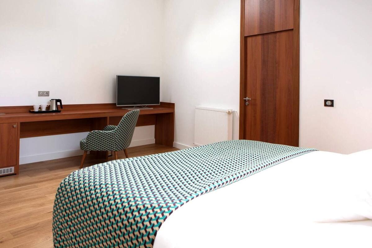 A bedroom with a bed, a desk with a television, a chair, and a radiator.