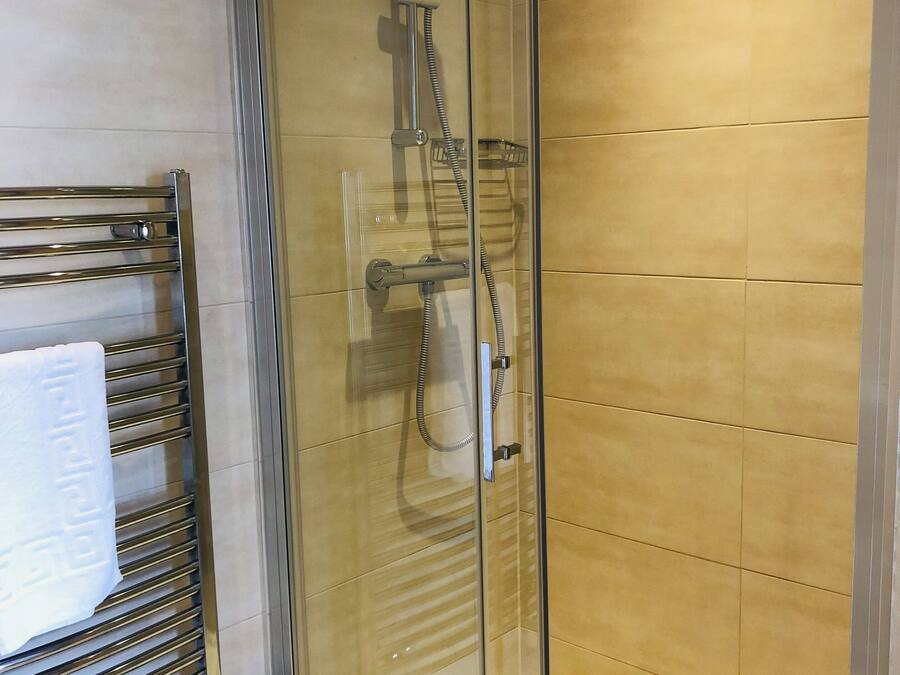 A glass-enclosed shower with a handheld showerhead and a handheld shower attachment.