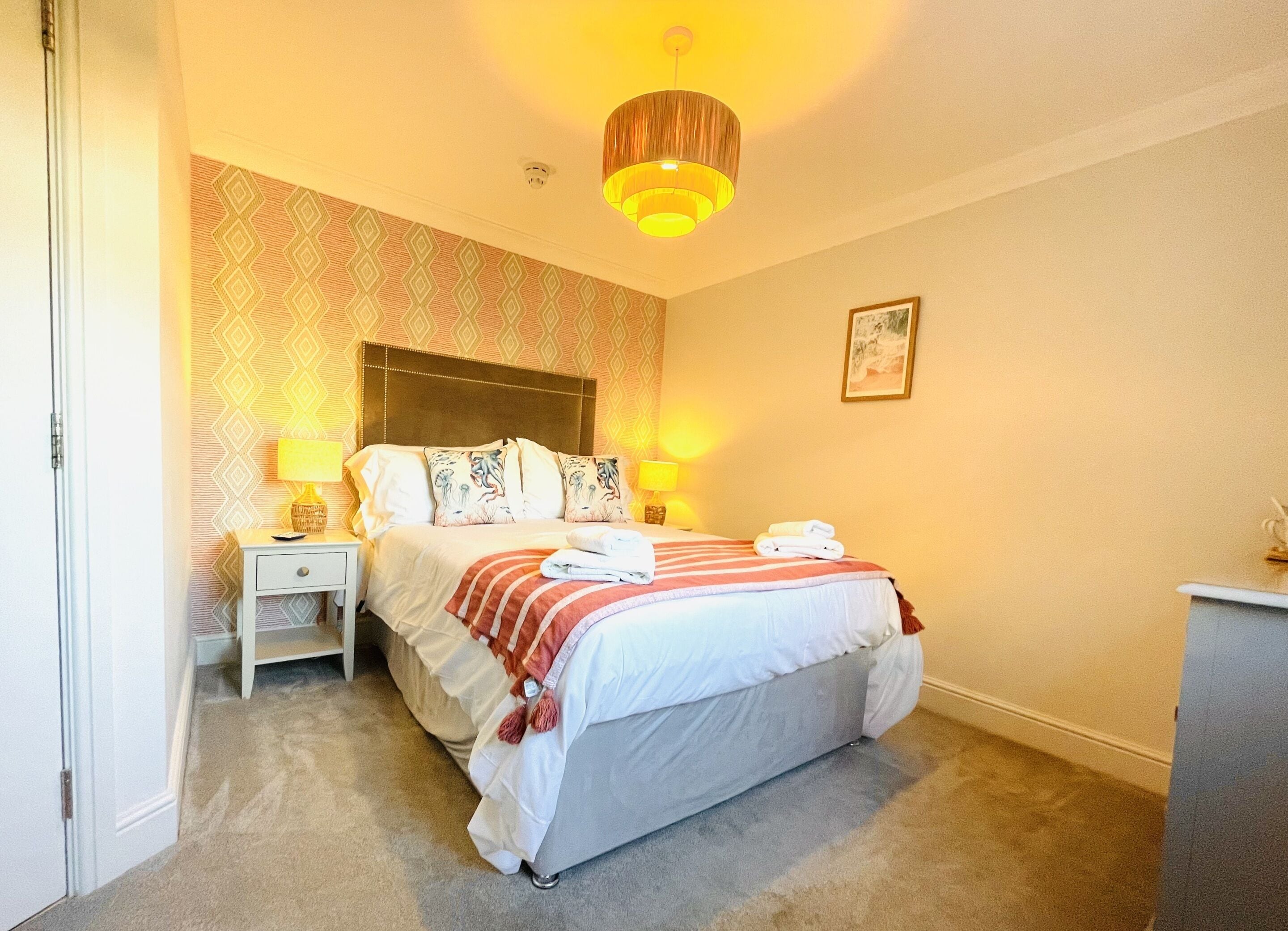 A neatly arranged bedroom with a bed, bedside lamps, a nightstand, and a small desk.