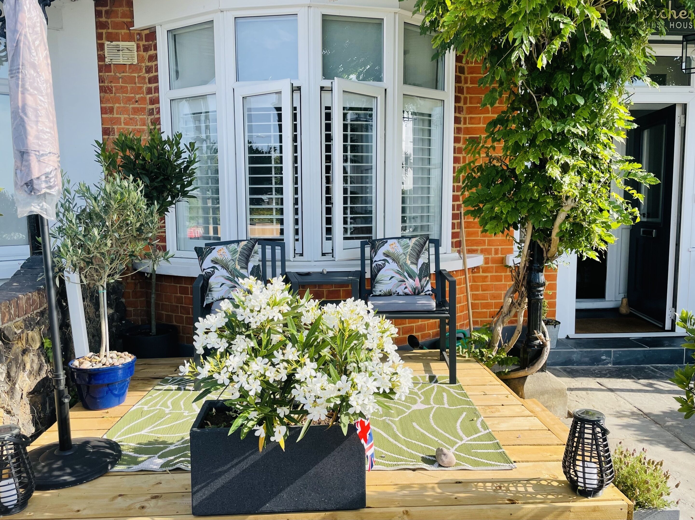 A cozy outdoor seating area with a wooden deck, a large flower planter, and a bench with cushions.