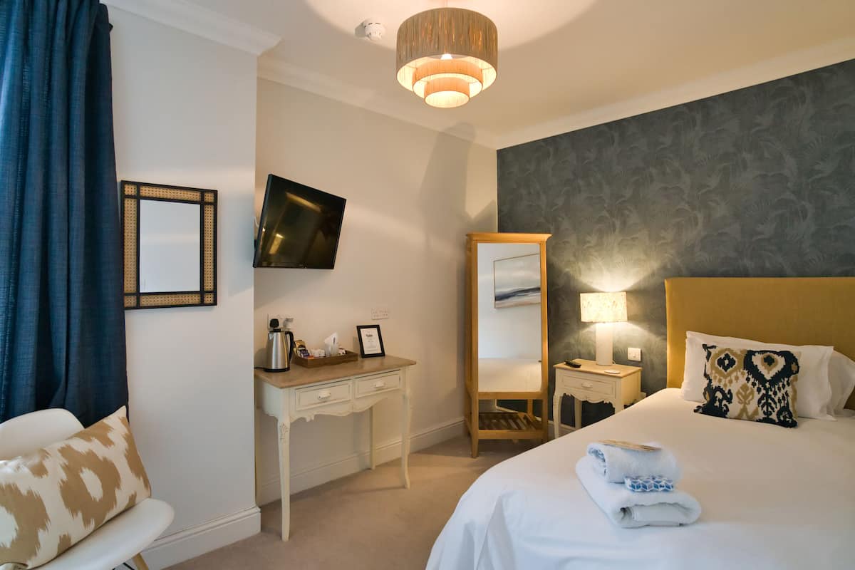 A hotel room with a bed, a desk, a chair, a TV, a mirror, and a lamp.