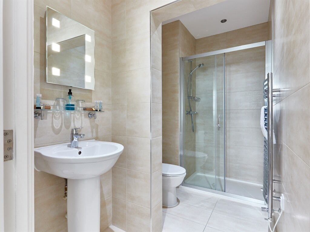 Un baño moderno con un lavamanos pedestal, cabina de ducha con mampara de vidrio y un inodoro.