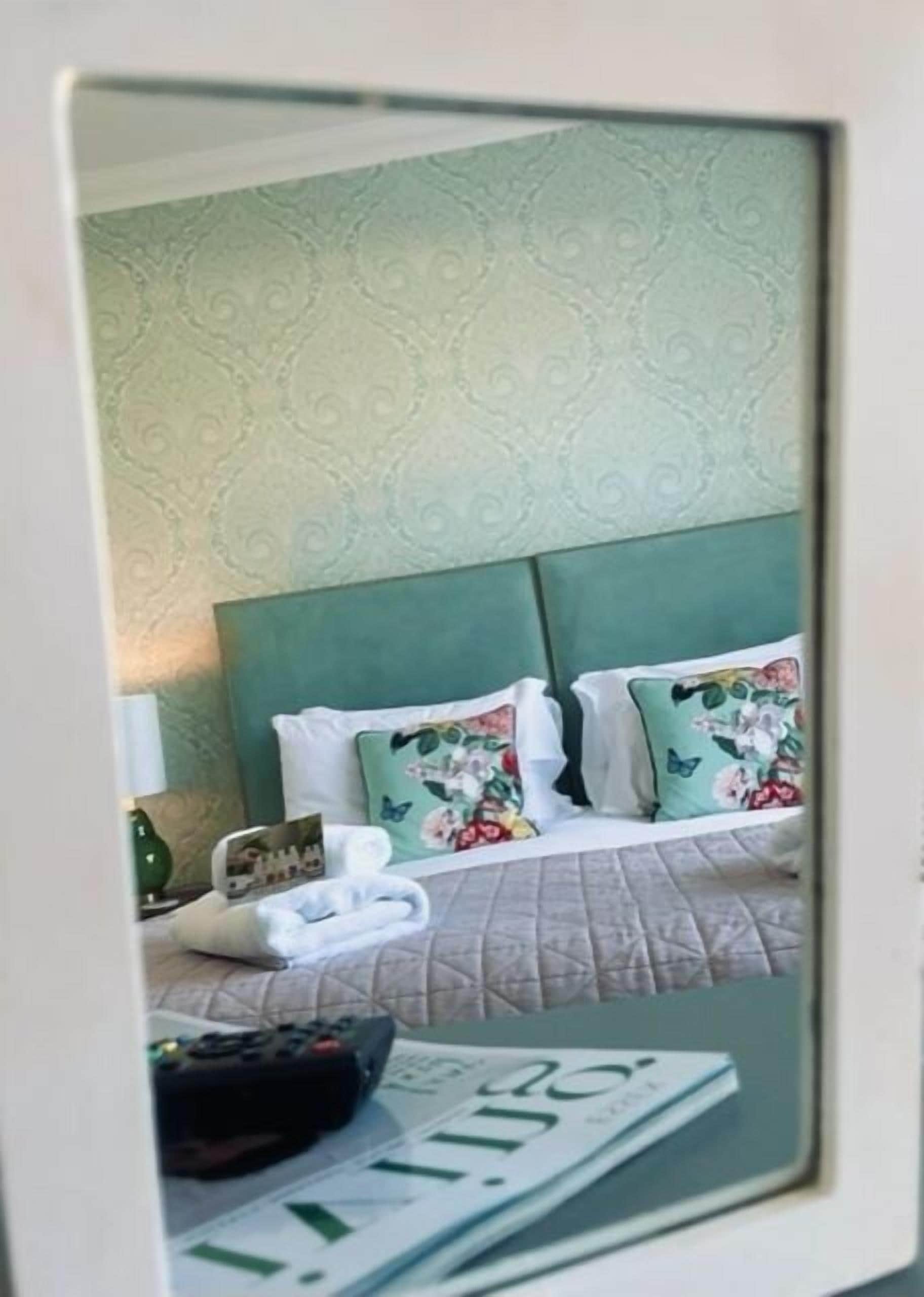 Quarto de hotel com cabeceira verde, almofadas florais, colcha acolchoada e um controle remoto na cama.