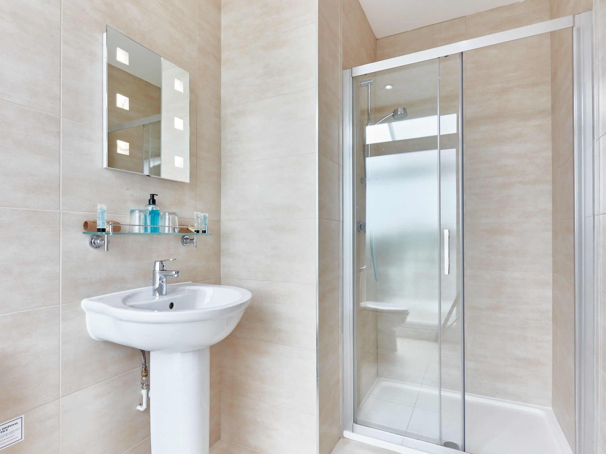 A modern bathroom with a white sink, a glass shower enclosure, and a mirror above the sink.