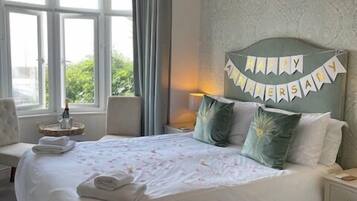 A neatly made bed with a 'Happy Anniversary' banner, a bedside lamp, and a view of greenery through the window.