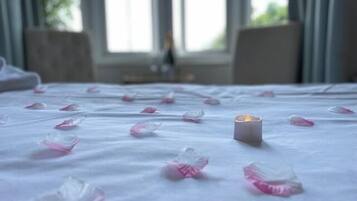 A bed with rose petals scattered across the surface and a lit candle in the center.