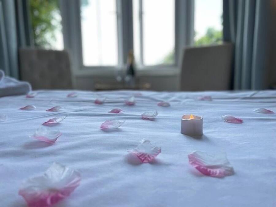 A bed with rose petals scattered across the surface and a lit candle in the center.