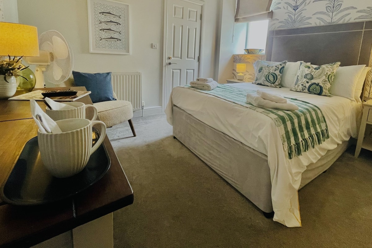 A neatly arranged bedroom with a bed, bedside tables, a chair, and a desk.