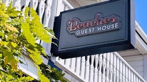 Skilt for 'Beaches Guest House' med et hvidt stakerværk i baggrunden.