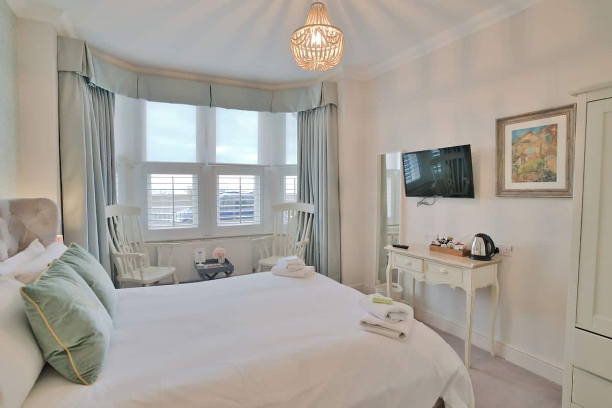 A hotel room with a large bed, a desk, a television, and a window with curtains.