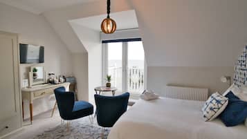 Une chambre à coucher comprenant un lit, deux chaises, un bureau, une télévision, une fenêtre avec vue et un luminaire suspendu.