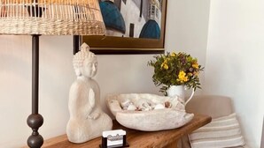 Et træskrivebord med en Buddha-figur, en lille Buddha-figur, en skål, en navneskilt, en lampe, en stol og en vase med blomster.