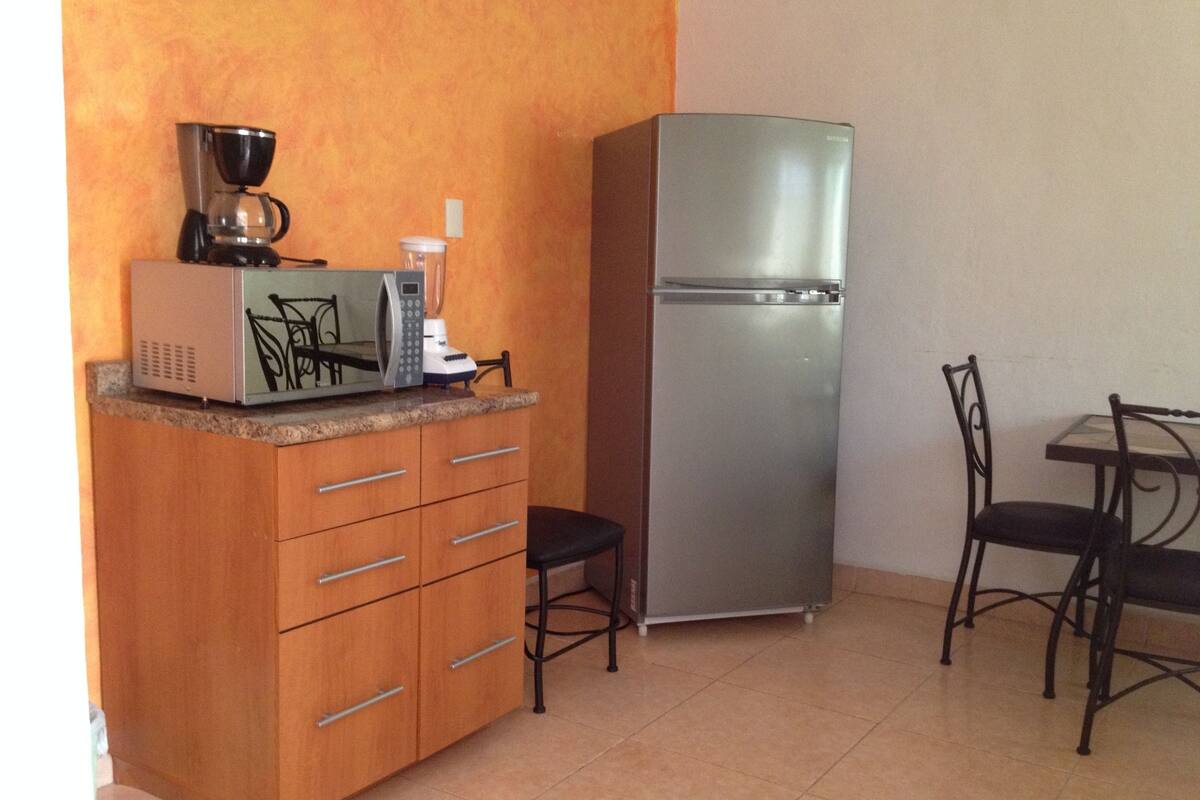 A compact kitchen with a microwave, coffee maker, and refrigerator. There are two chairs and a small table.
