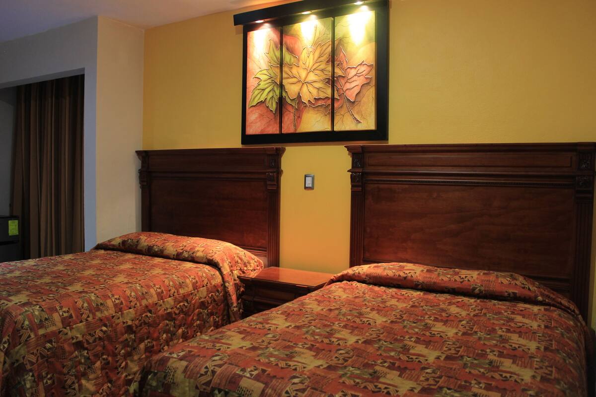 A hotel room with two beds, wooden headboards, and a floral artwork above the beds.