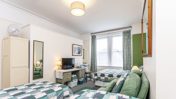 Camera d'albergo con due letti, una scrivania con televisore, una sedia e una finestra con tende.