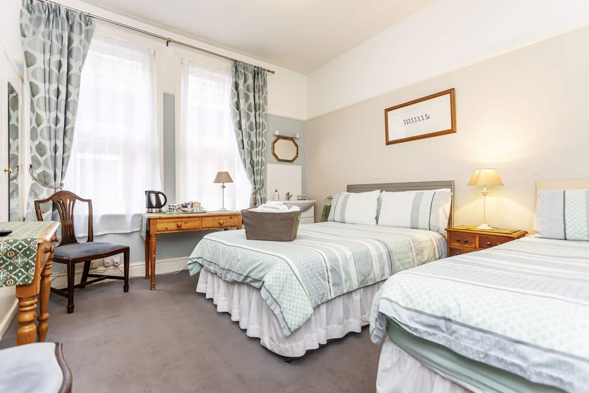 A bedroom with two beds, a desk, a chair, and a bedside table with lamps.